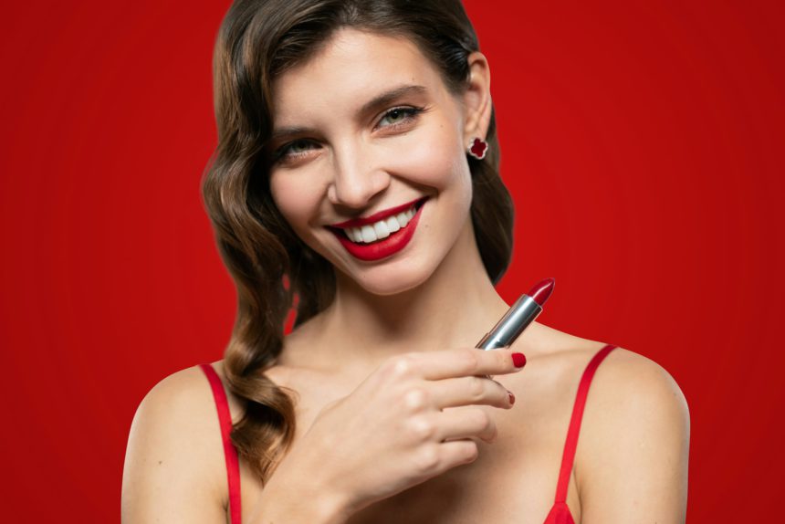 Portrait of elegant woman with red lips and evening makeup holding lipstick
