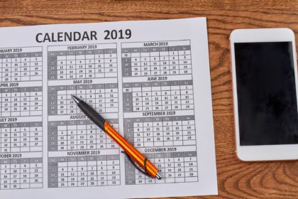 Year calendar with smartphone and pen on wooden desk.